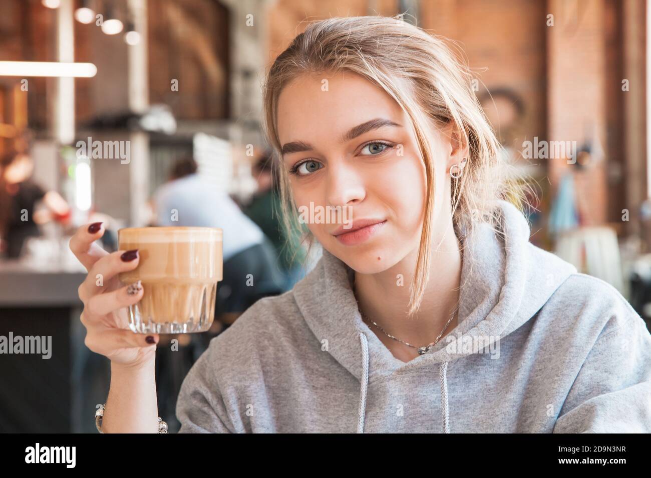 Giovane bionda bella ragazza europea tiene un bicchiere di caffè bianco piatto. Primo piano con messa a fuoco morbida selettiva Foto Stock