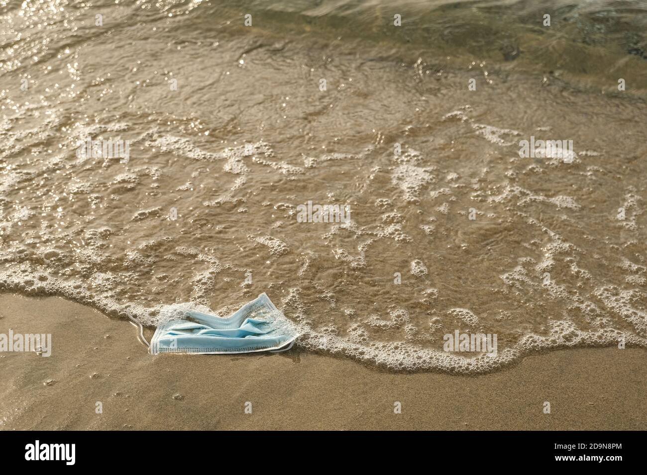 Scartato maschera chirurgica che galleggia sulla riva del mare sporco, covid19 pandemia inquinamento Foto Stock