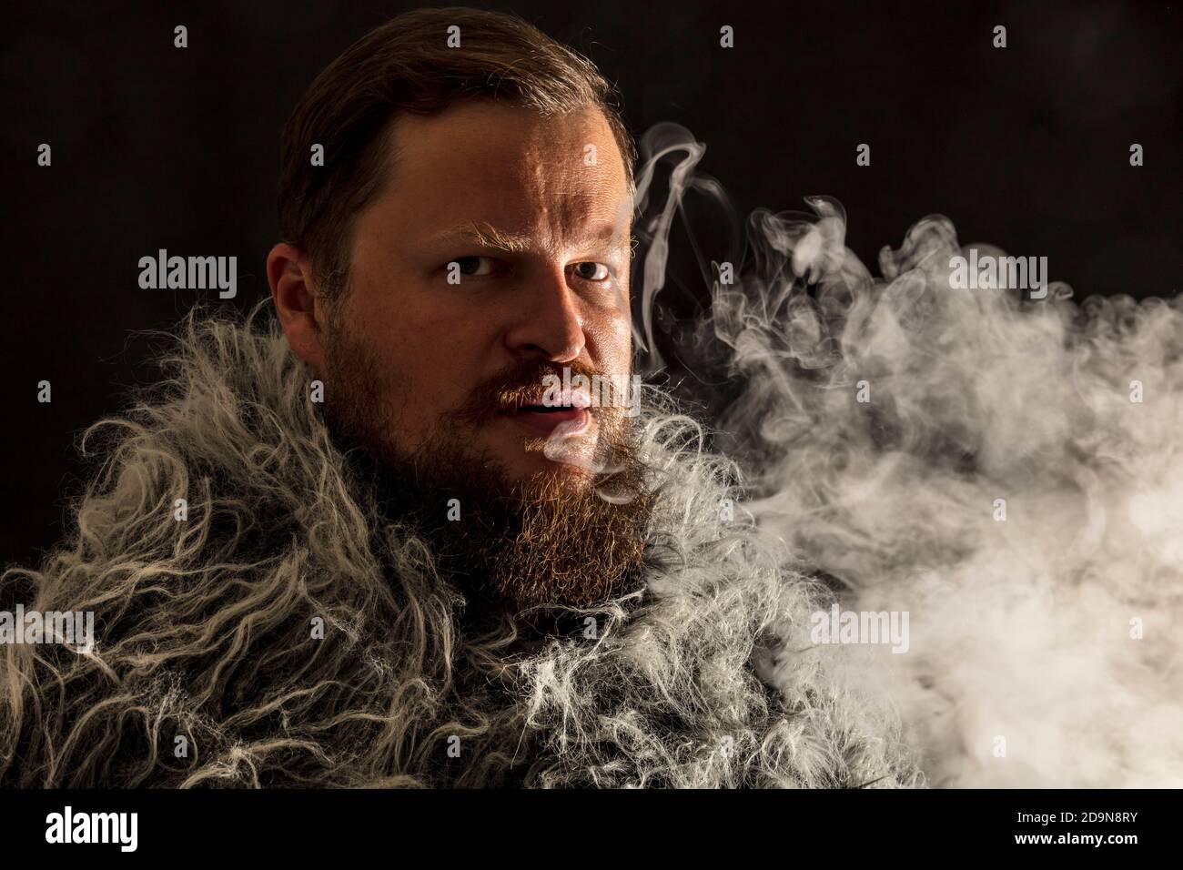 Uomo dal bearded solido vestito con un mantello di pelliccia che esala vapore dal suo ritratto di studio di bocca Foto Stock