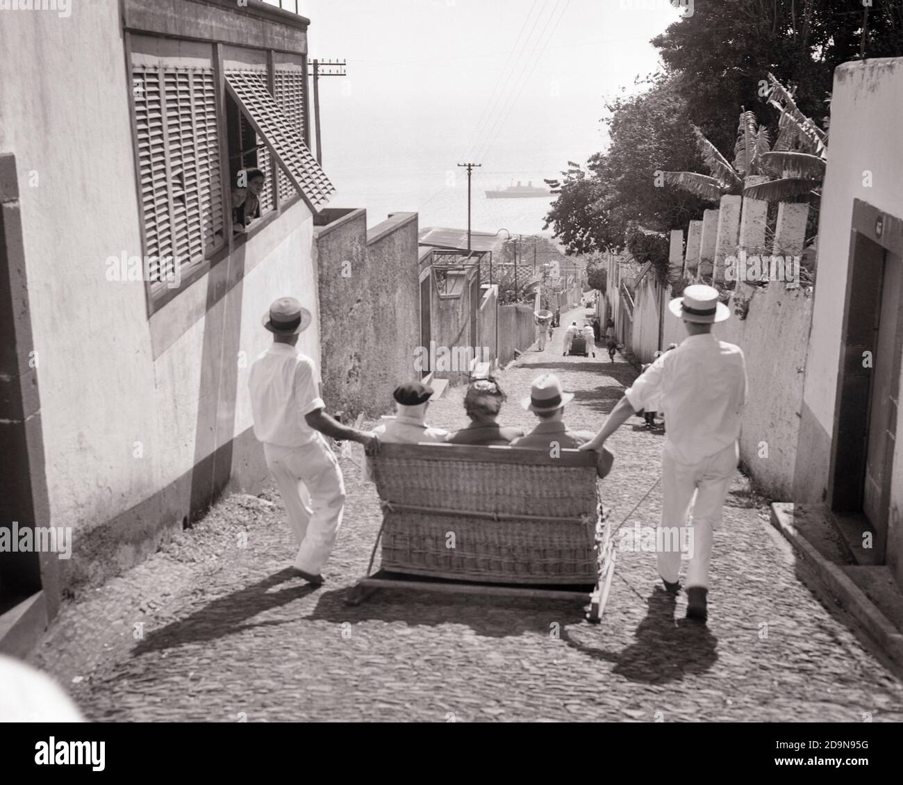 ANNI '50 DUE UOMINI CARREIROS CHAUFFEURS GUIDA TRE TURISTI IN UN ESCURSIONE IN TOBOGA DI MONTE SLED IN VIMINI A FUNCHAL MADEIRA PORTOGALLO - R15493 RGE001 HARS EUROPE B&W TOBOGGAN AVVENTURA AD ALTO ANGOLO IN DISCESA ISOLE EUROPEE ATTRAZIONI TURISTICHE OCCUPAZIONI SLED RIPIDO ANONIMO MADEIRA ATLANTICO OCEAN MONTE PORTUGAL CAVALCARE SOLUZIONI IN BIANCO E NERO CON PENDENZA VECCHIA ALLA MODA Foto Stock