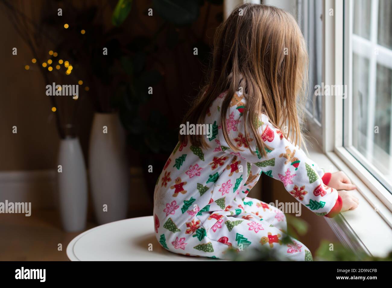 Giovane ragazza guarda fuori finestra mentre indossa pigiami di Natale Foto Stock