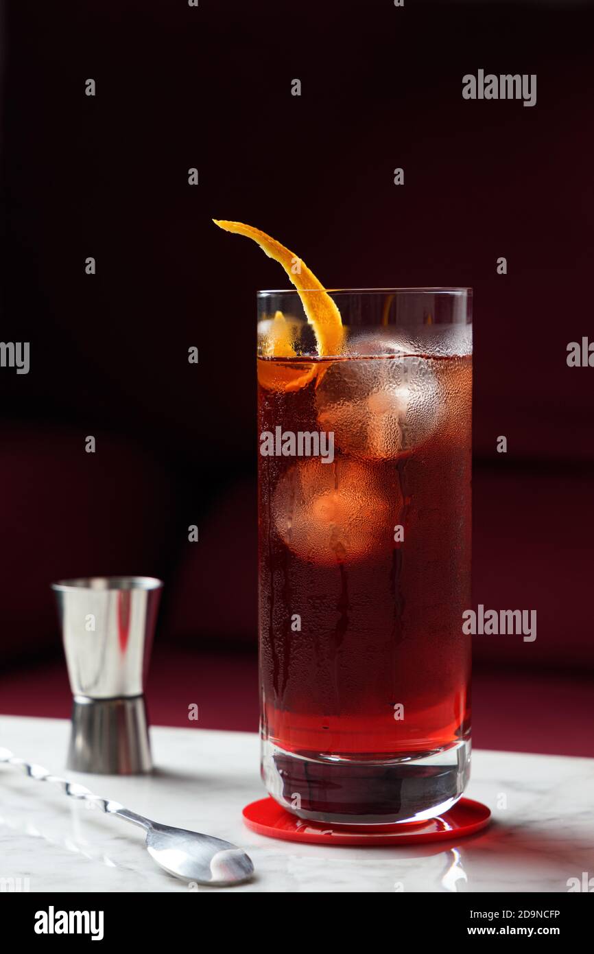 American cocktail con Orange Twist su un tavolo in marmo. Divano rosso come sfondo. Vista frontale Foto Stock