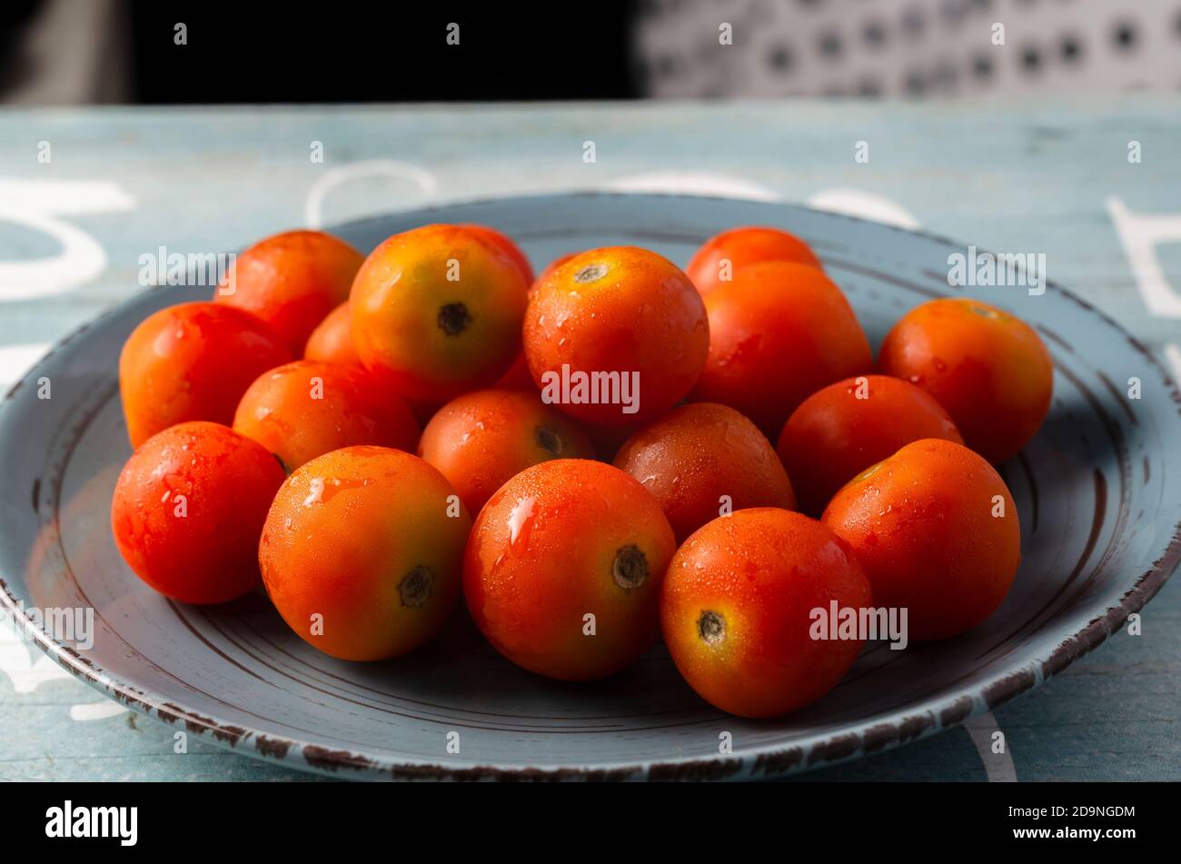 Piatto pieno di pomodori ciliegini freschi su un blu a contrasto sfondo turchese Foto Stock