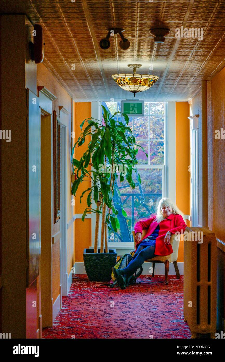 Donna che si rilassa nella sedia del corridoio, James Bay Inn, Victoria, British Columbia, Canada Foto Stock