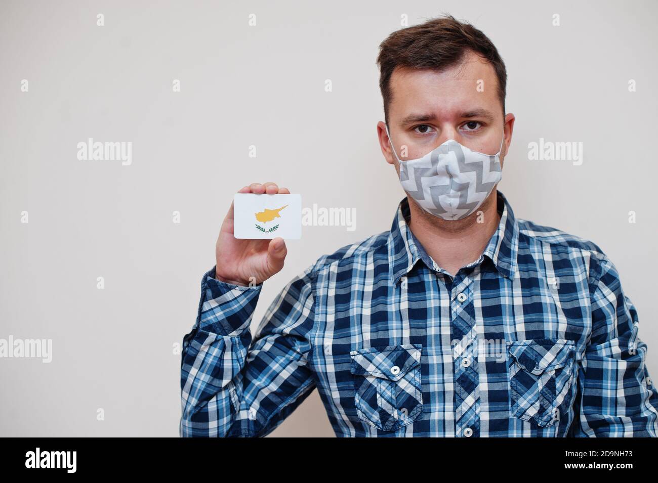 Uomo in camicia a scacchi mostra carta bandiera Cipro in mano, indossare maschera di protezione isolato su sfondo bianco. Paesi asiatici concetto di Coronavirus. Foto Stock