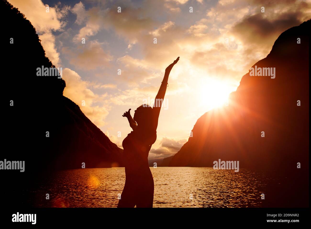 Silhouette di una donna con le braccia allungate all'alba da un lago Foto Stock