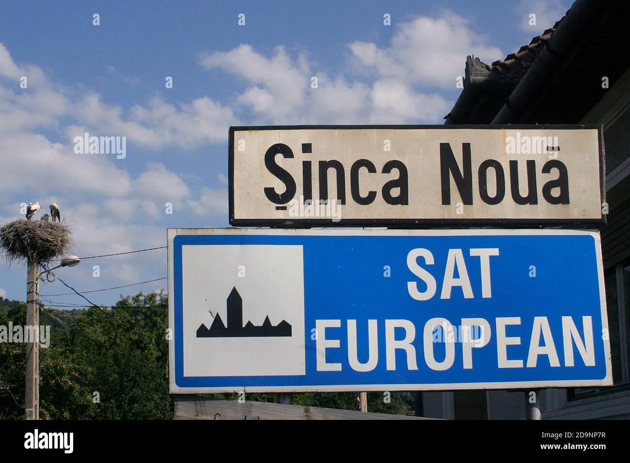Contea di Brasov, Romania. Segnale stradale all'ingresso di Sinca Nouna, designato come "villaggio europeo" dalla Commissione europea nel 2005. Nido di cicogna. Foto Stock