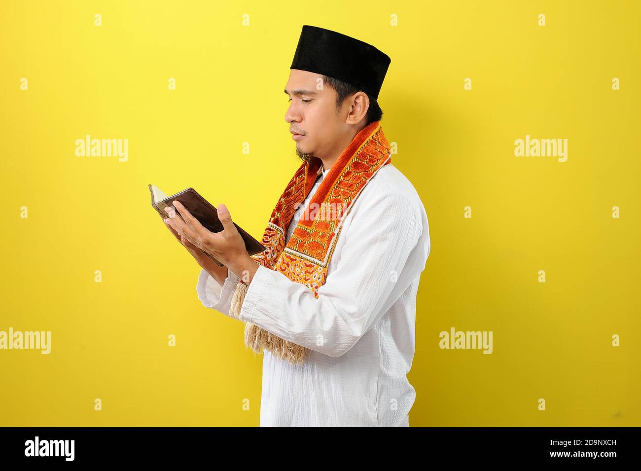 Ritratto di giovane musulmano asiatico che legge il Corano, isolato su sfondo giallo Foto Stock