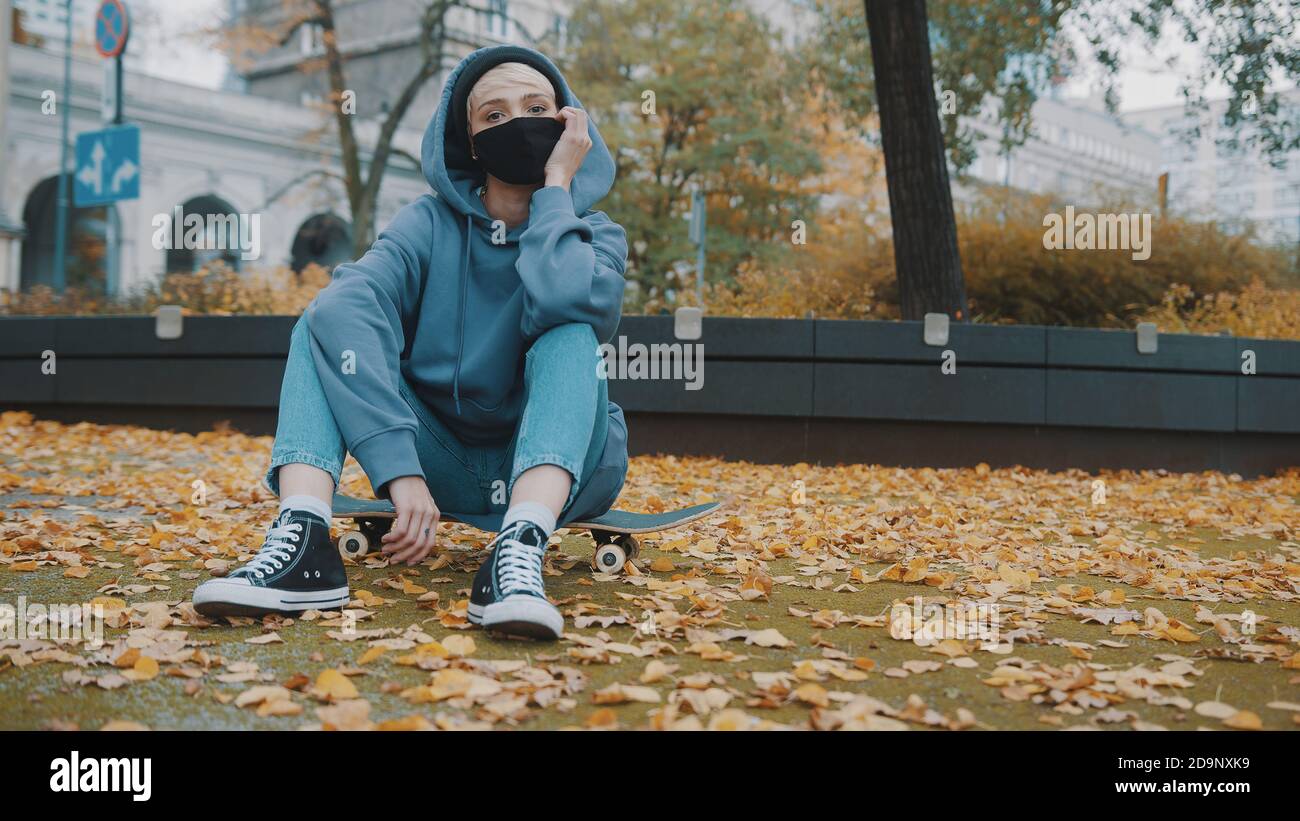 Giovane donna hispter con maschera facciale e felpa con cappuccio seduta  sullo skateboard nel parco cittadino in autunno. Foto di alta qualità Foto  stock - Alamy