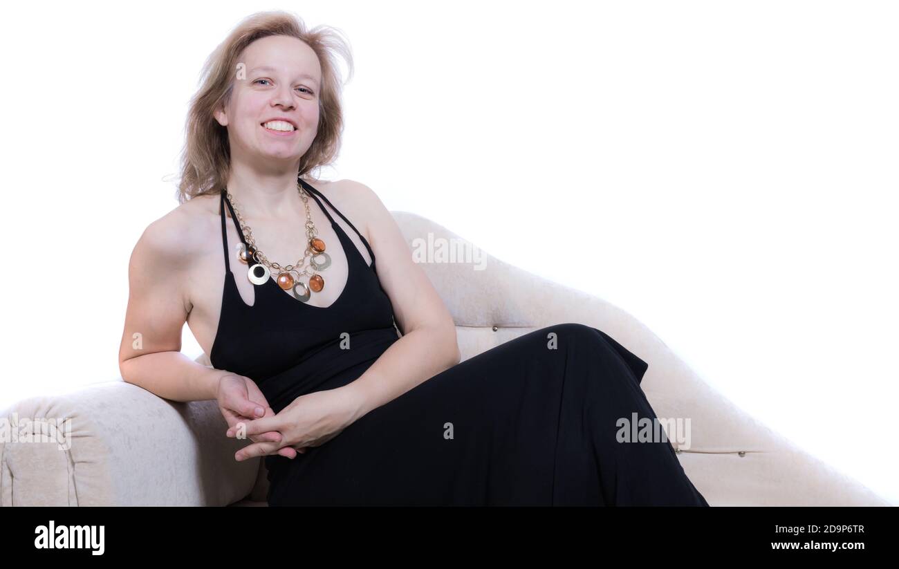 Allegra donna di 40 anni in abito nero seduta su divano studio ritratto su sfondo bianco Foto Stock