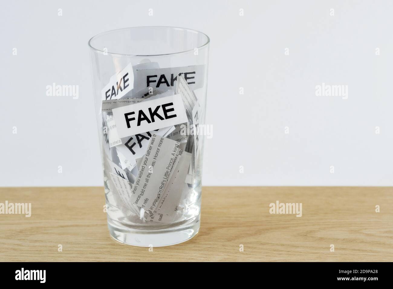 Vetro dell'acqua con i pezzi di carta con le notizie ed il Word Fake - concetto di notizie false Foto Stock