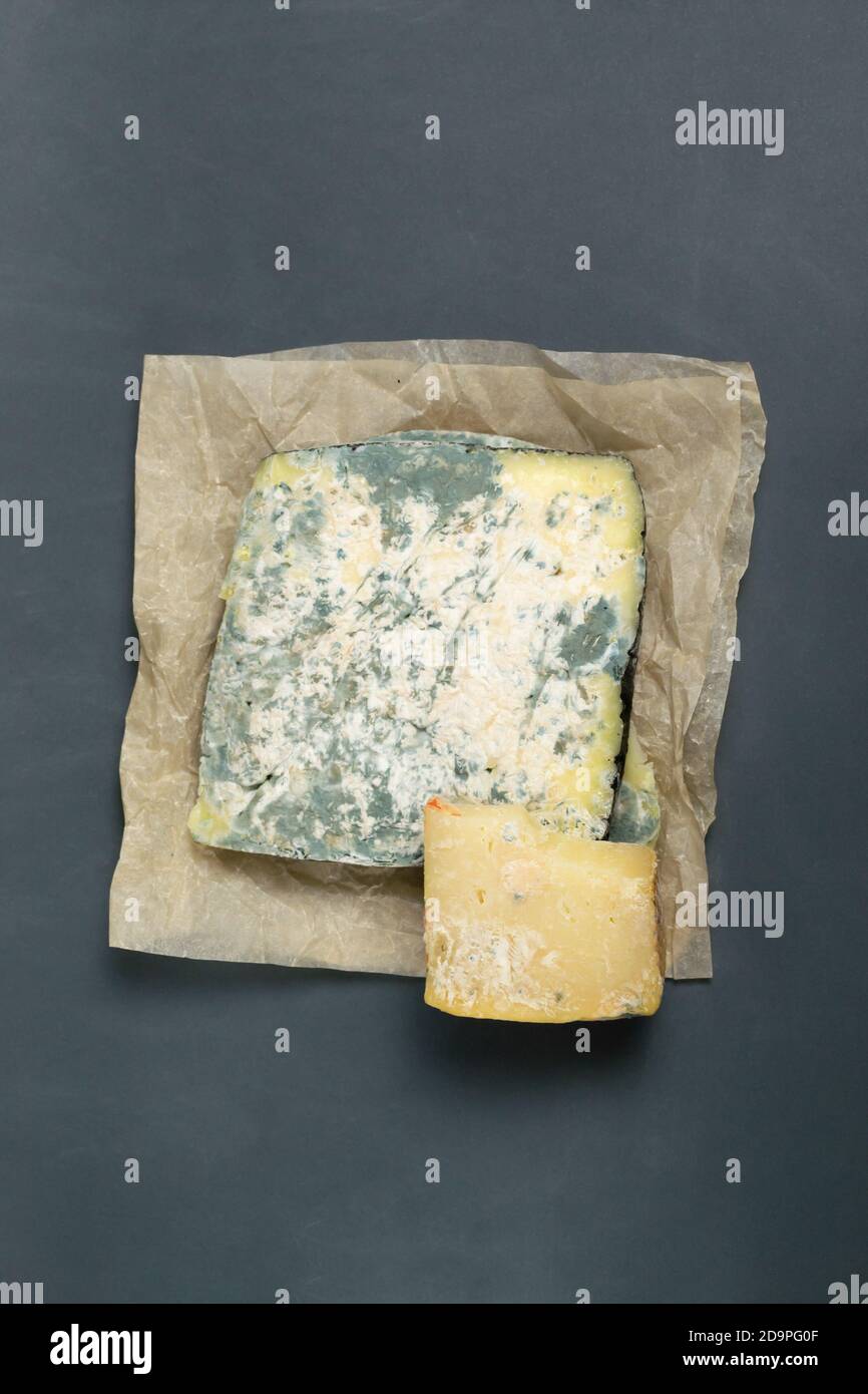 Diversi pezzi di formaggio guastato su sfondo grigio. Concetto di spreco di cibo. Orientamento verticale. Vista dall'alto. Spazio di copia. Foto Stock