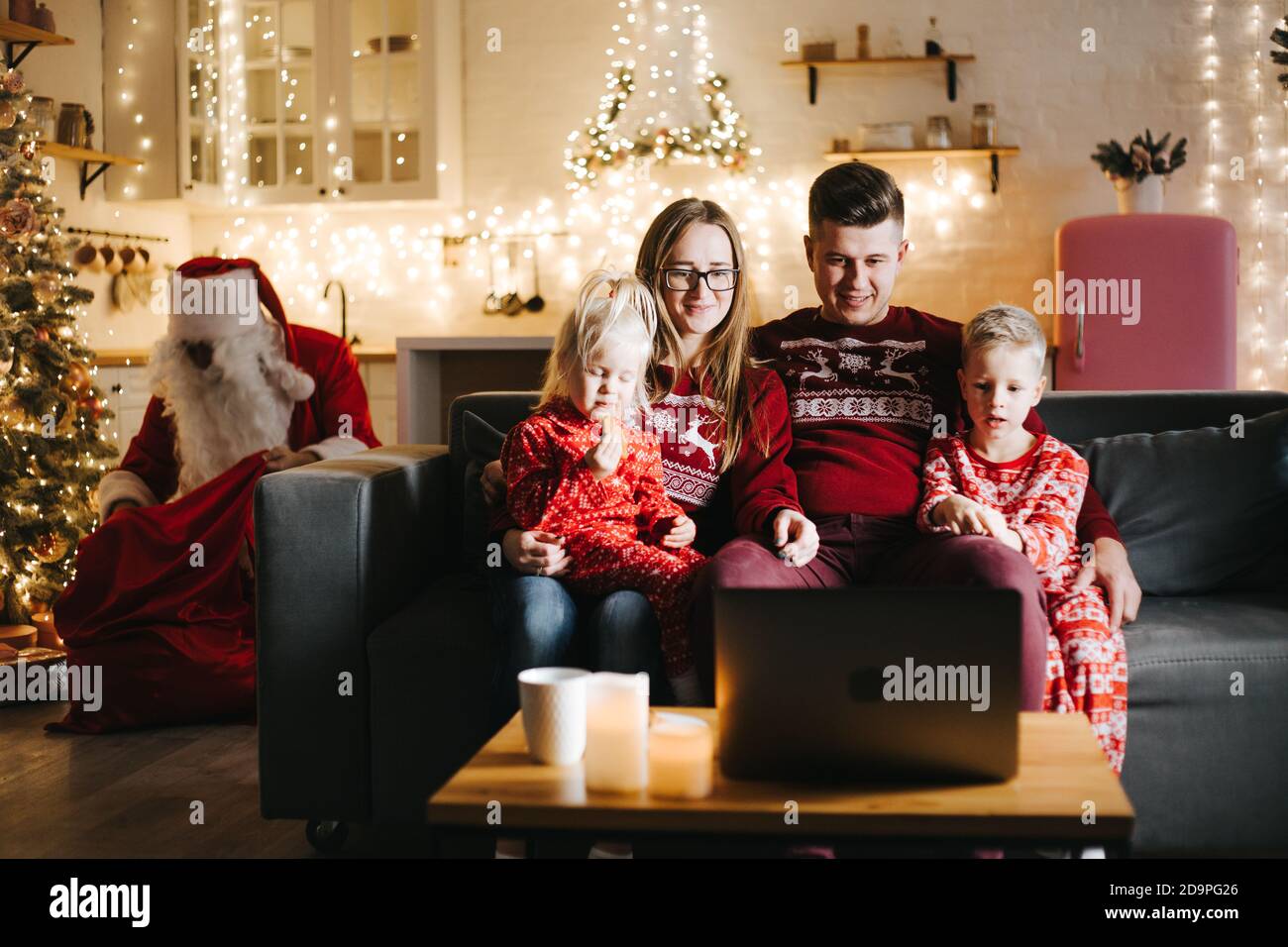 Babbo Natale mettendo i regali sotto l'albero di Natale in camera con famiglia Foto Stock