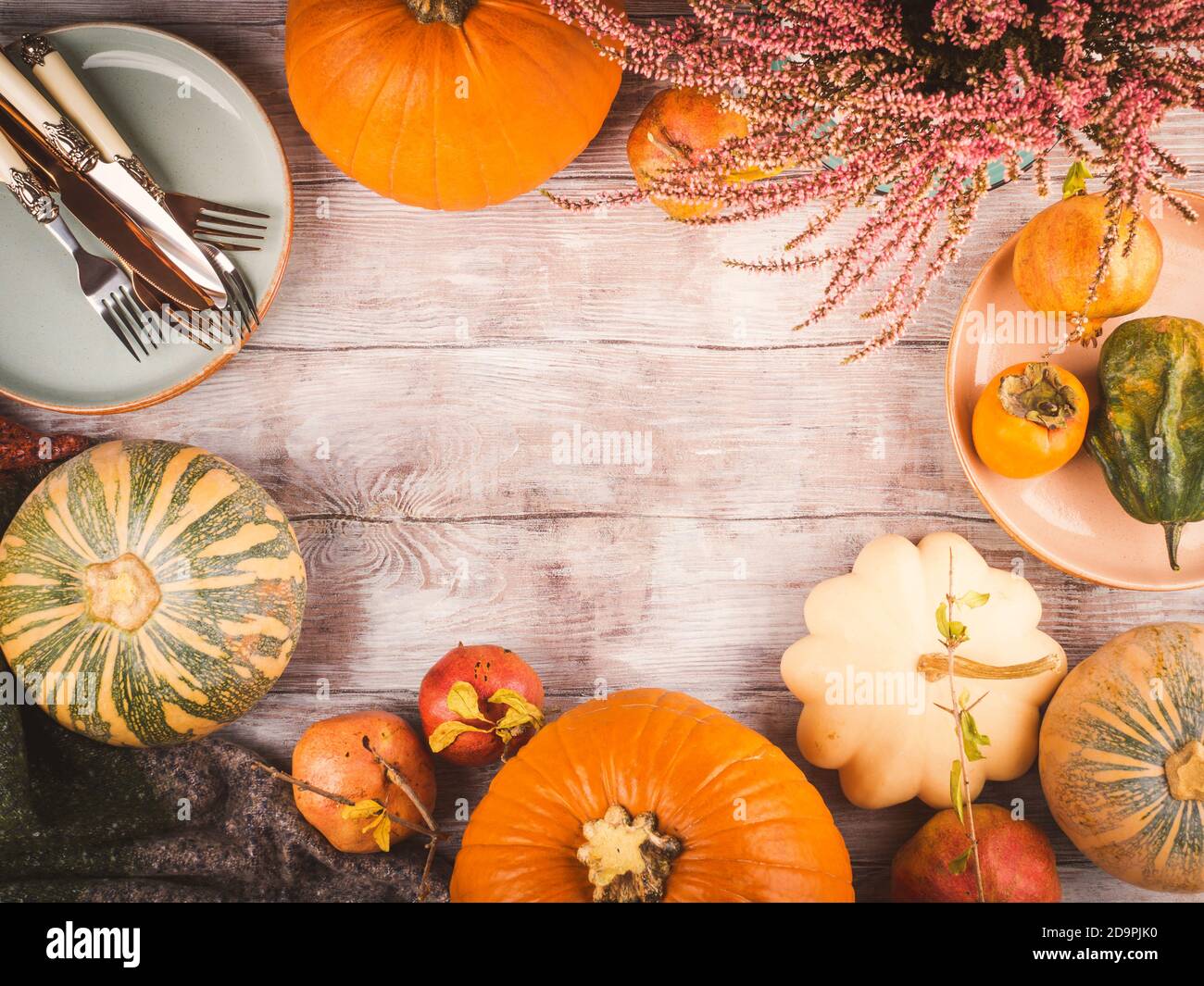 Sfondo in legno di ringraziamento autunnale con zucche, frutta di caduta e piatti con argenteria per cena Foto Stock