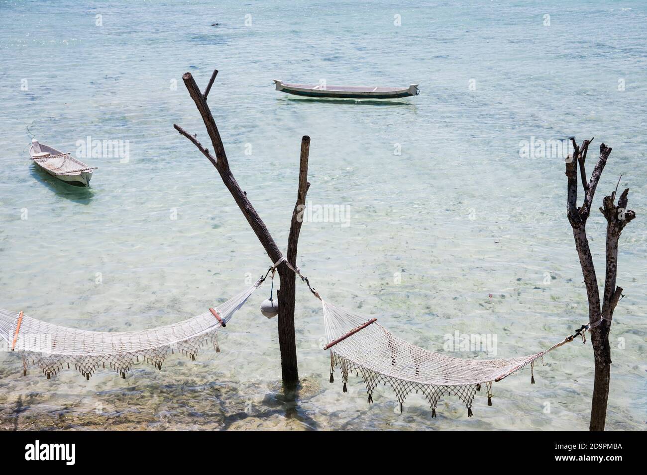 Due amache appese agli alberi sulle acque cristalline tropicali di Bali, mare trasparente e due piccole barche. Viaggio da sogno destinazione relax vacanza Foto Stock