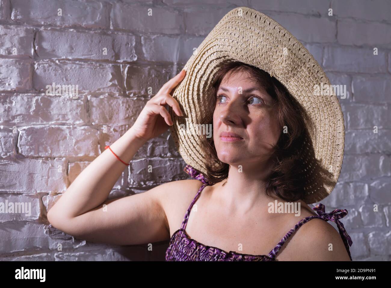 Allegra donna di 40 anni in cappello largo-brimmed e viola abito studio ritratto su muro di mattoni sfondo Foto Stock
