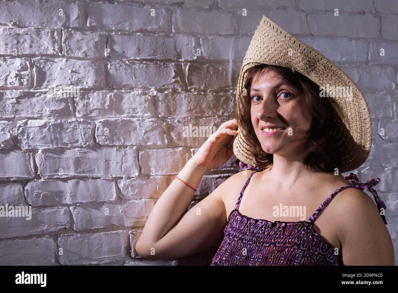Allegra donna di 40 anni in cappello largo-brimmed e viola abito studio ritratto su muro di mattoni sfondo Foto Stock