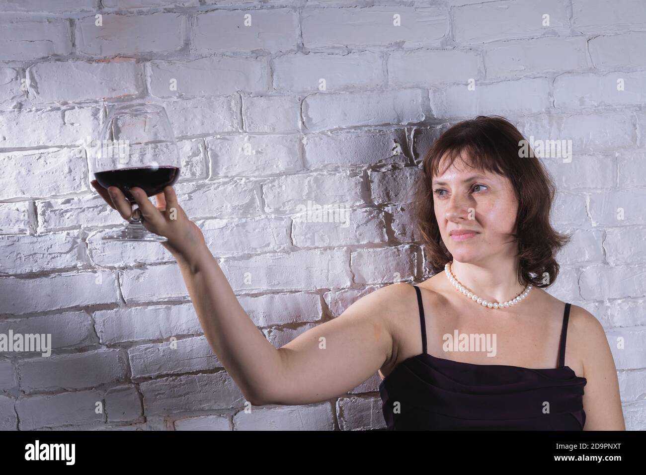Allegra donna di 40 anni in abito classico con vetro di studio del vino ritratto su muro di mattoni sfondo Foto Stock