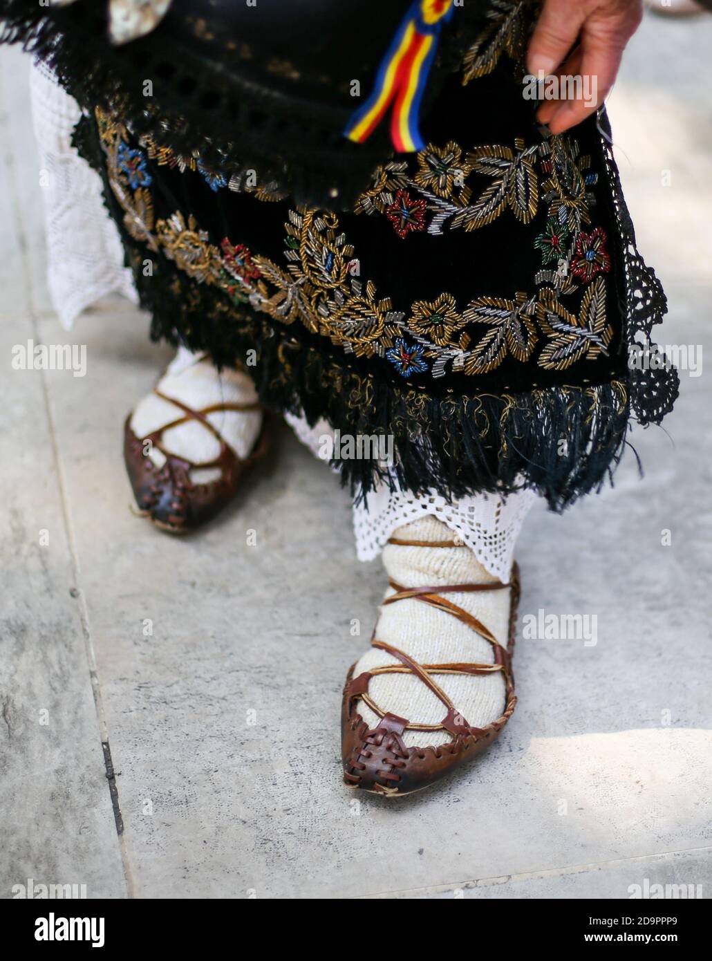 Profondità di campo bassa (fuoco selettivo) immagine con le scarpe contadine tradizionali rumene (opinci) ai piedi di una donna anziana. Foto Stock
