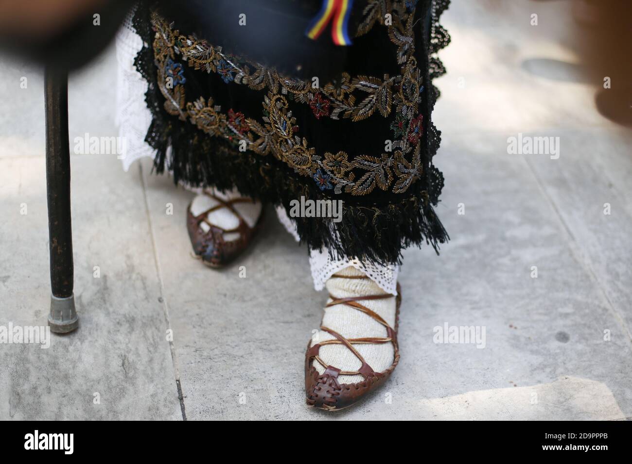Profondità di campo bassa (fuoco selettivo) immagine con le scarpe contadine tradizionali rumene (opinci) ai piedi di una donna anziana. Foto Stock