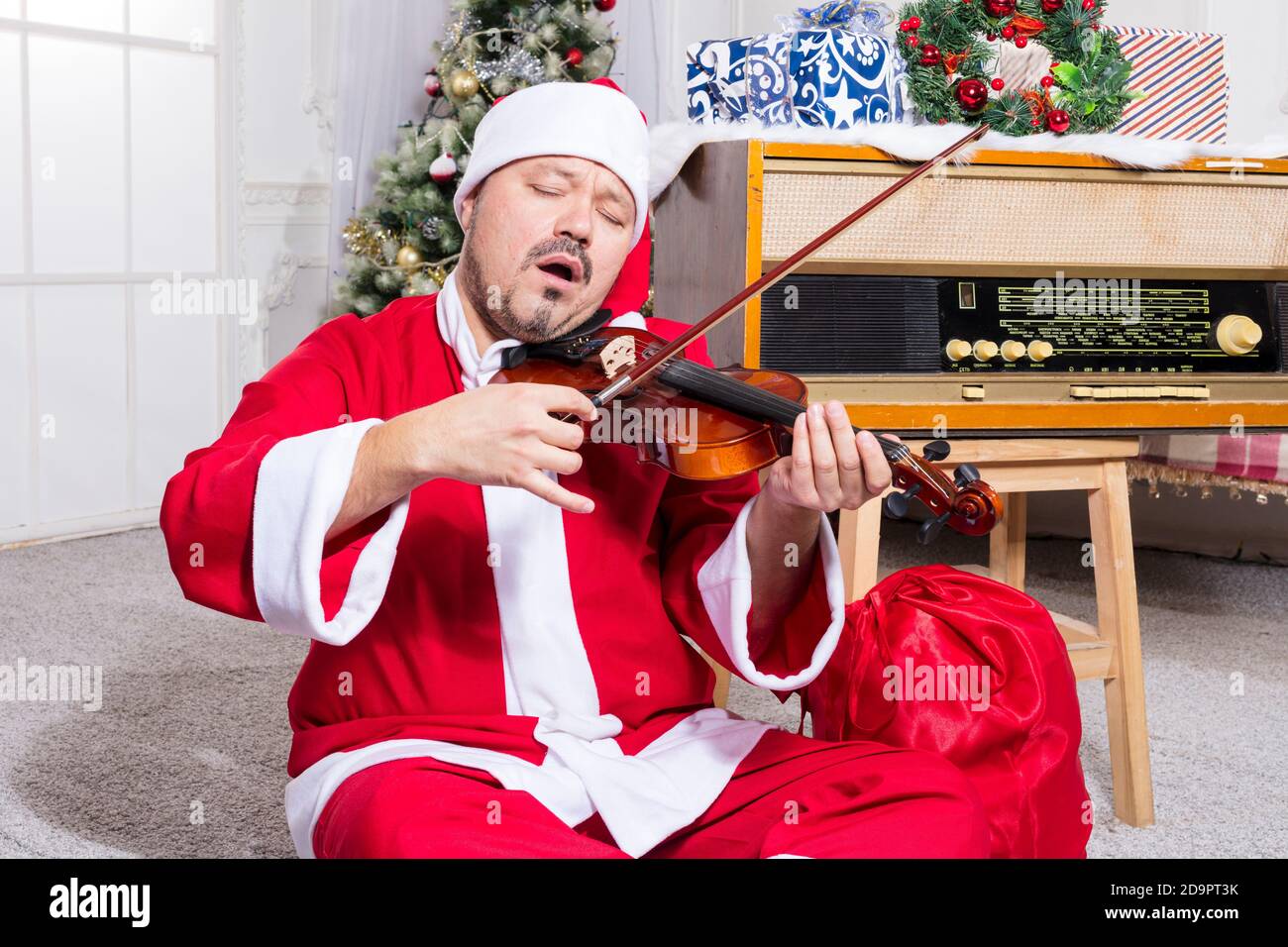 Uomo bearded vestito in costume di Babbo Natale che gioca studio di violine verticale Foto Stock