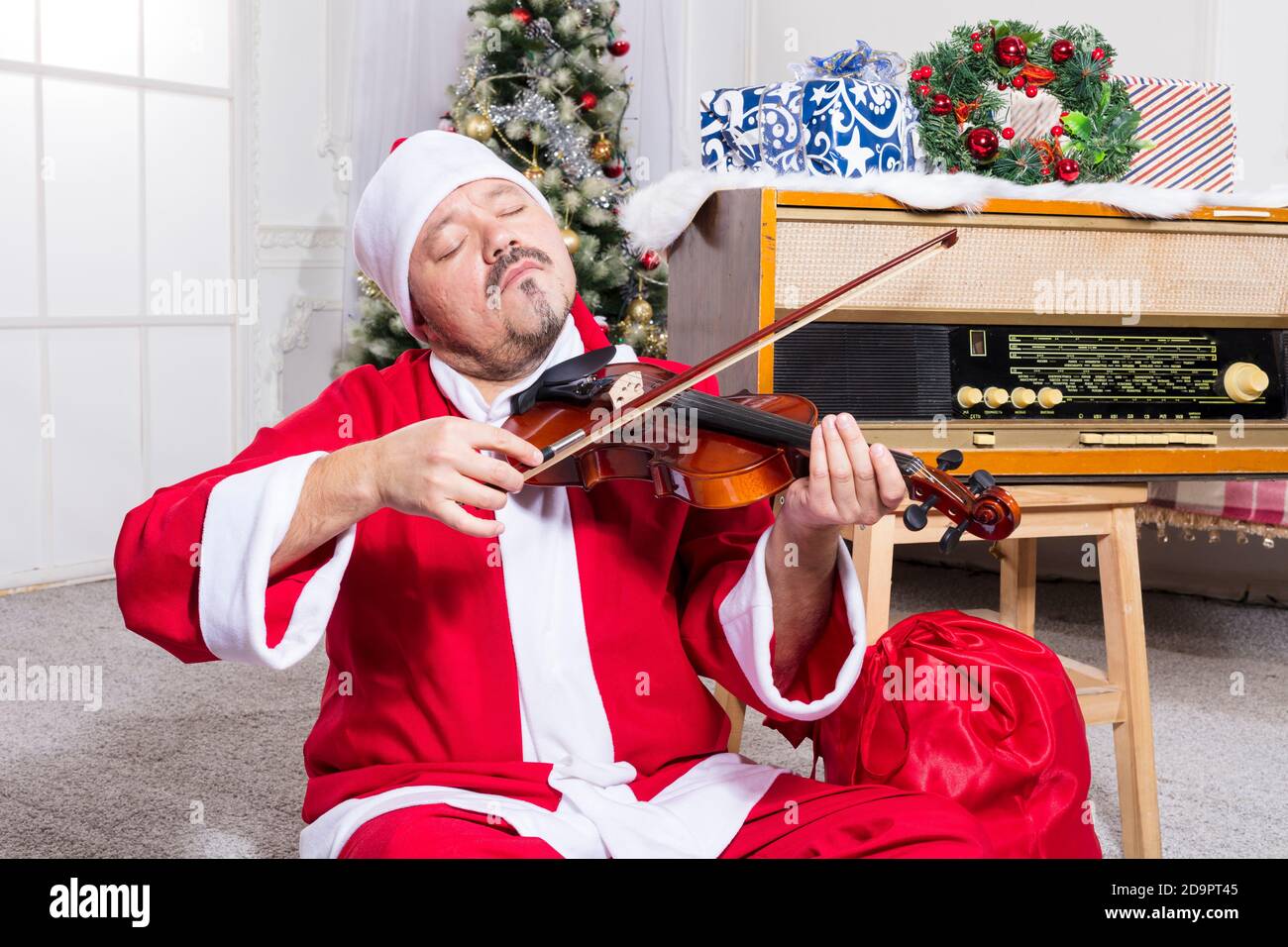 Uomo bearded vestito in costume di Babbo Natale che gioca studio di violine verticale Foto Stock