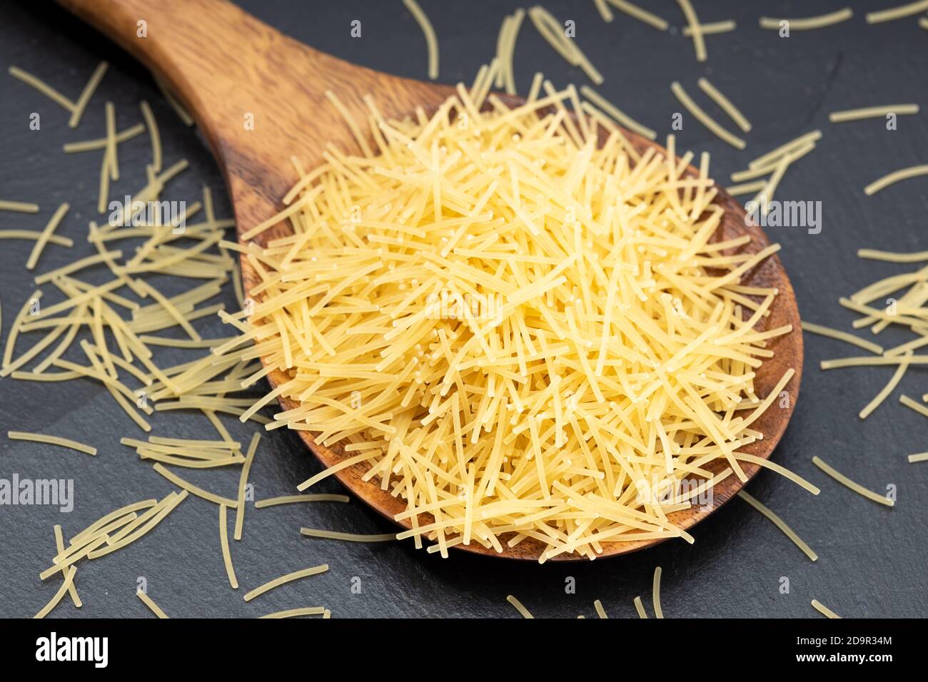 Zuppa non cotta, pasta da noodle in un cucchiaio di legno su un tavolo scuro. Foto Stock