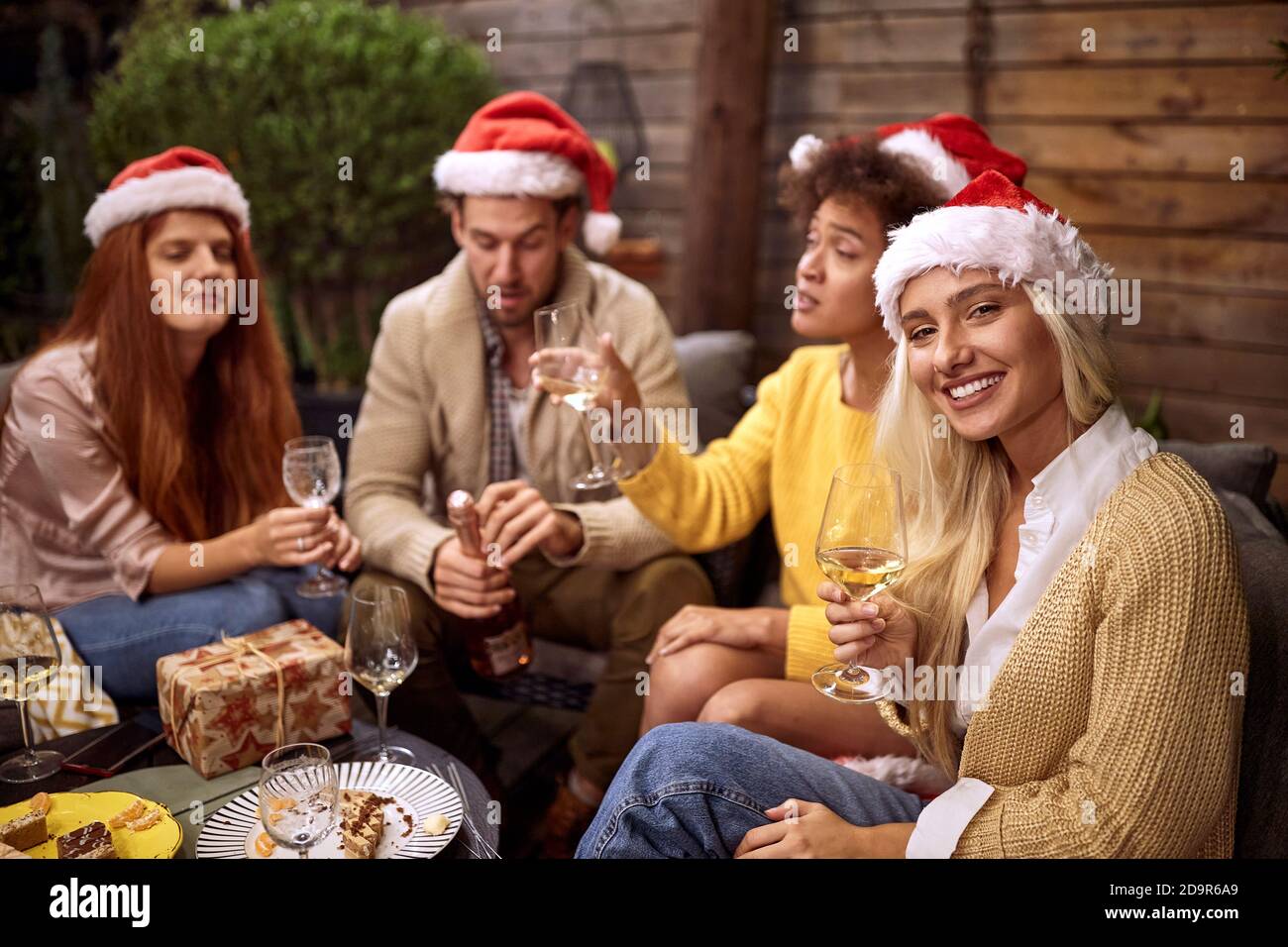 bella bionda guardando la macchina fotografica con i suoi amici sullo sfondo, bere vino bianco, festeggiare il natale Foto Stock