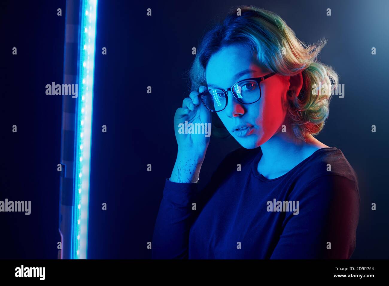 Ritratto di giovane ragazza alternativa in occhiali con capelli verdi in luce al neon rosso e blu in studio Foto Stock