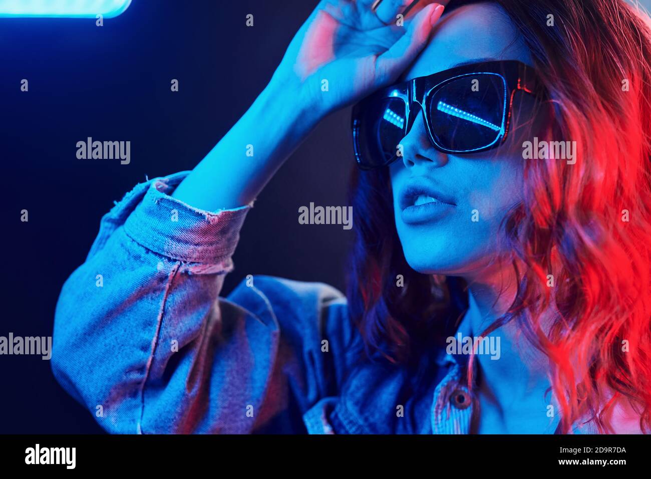 Ritratto di giovane ragazza in occhiali da sole in rosso e blu neon in studio Foto Stock
