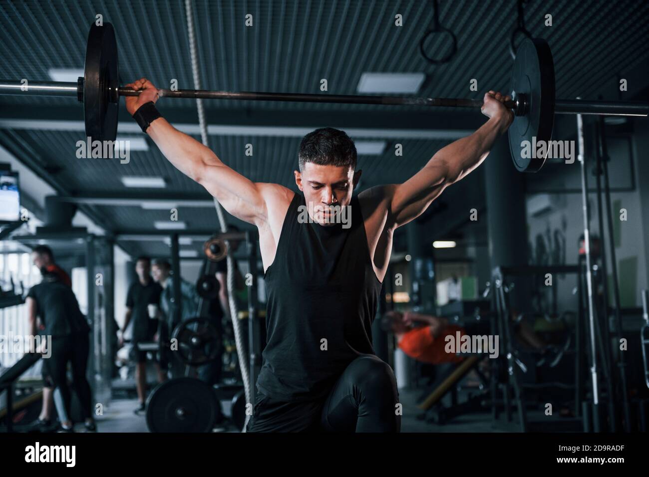 Forte giovane uomo in abiti sportivi facendo esercizi con pesante pesi in palestra Foto Stock
