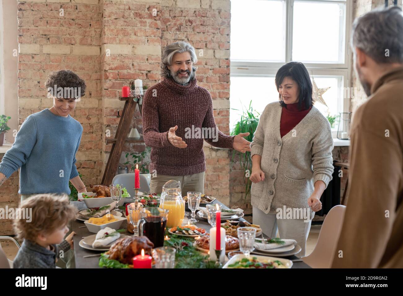 Felice uomo maturo in casualwear aiutare i membri della famiglia a prendere i loro luoghi Foto Stock