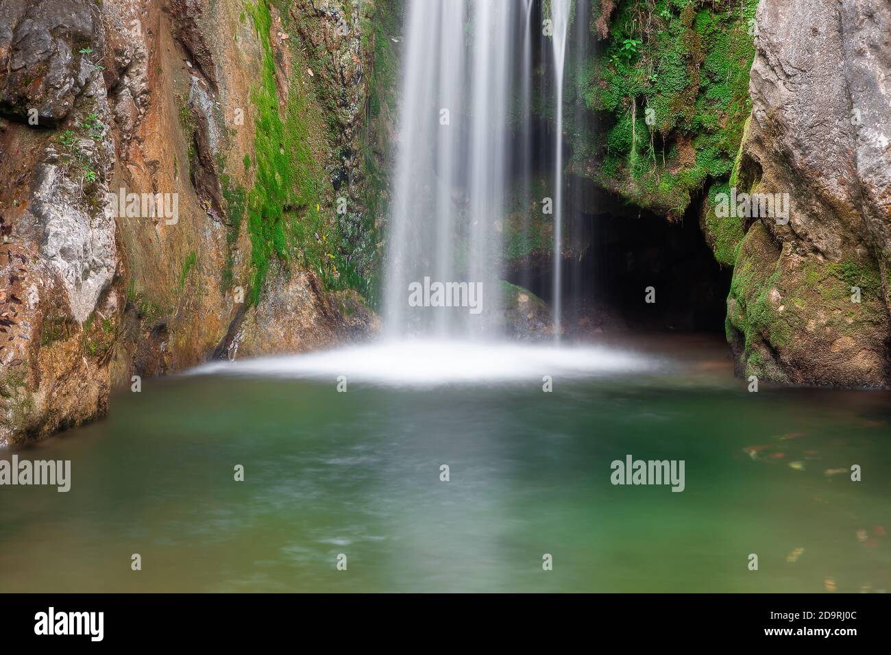 Cascata panoramica in canyon roccioso, acqua verde in primo piano con foglie colorate d'autunno e muschio vivido sulle scogliere bagnate Foto Stock