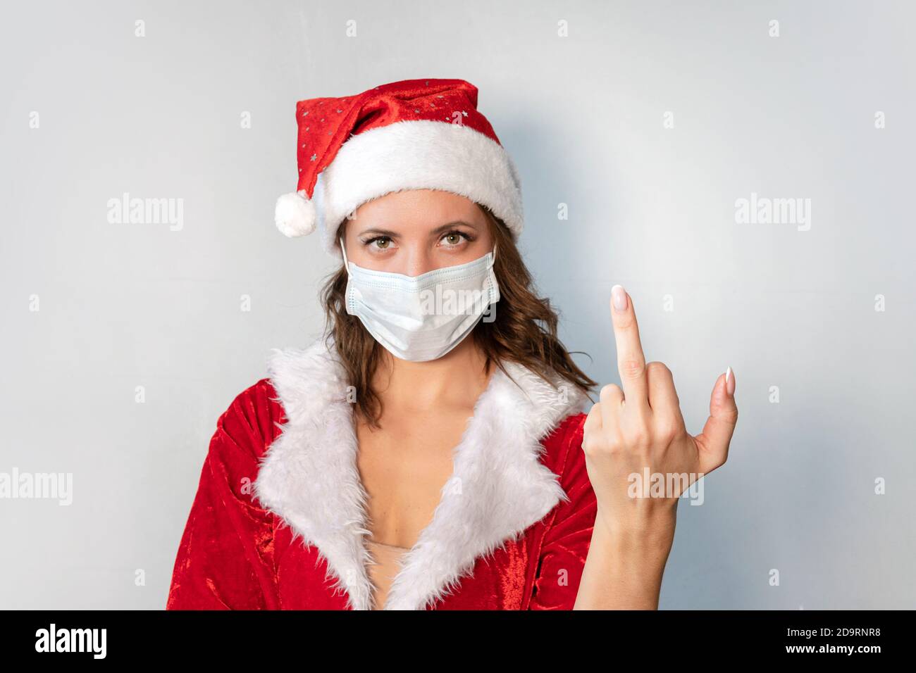Bella giovane donna in costume rosso di Babbo Natale e maschera medica protettiva contro il virus. Concetto di celebrare il Natale in covid 19 pandemia e. Foto Stock