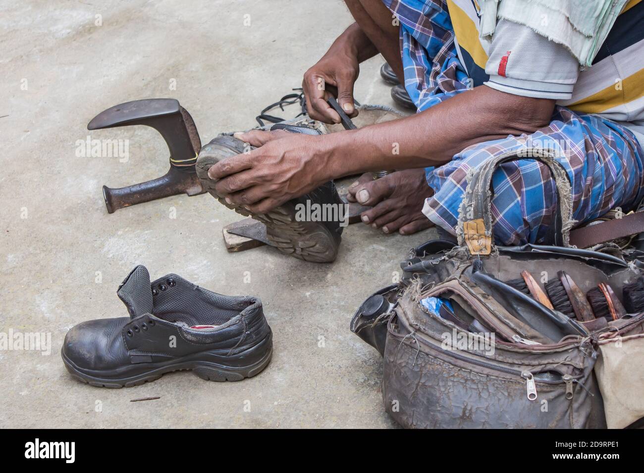 Indiano locale acciottolato riparazione scarpe accanto strada a mano utilizzando gli attrezzi in modo tradizionale. Naturale colpo raffigurante lavoro quotidiano di un regolare acciottolo. Foto Stock
