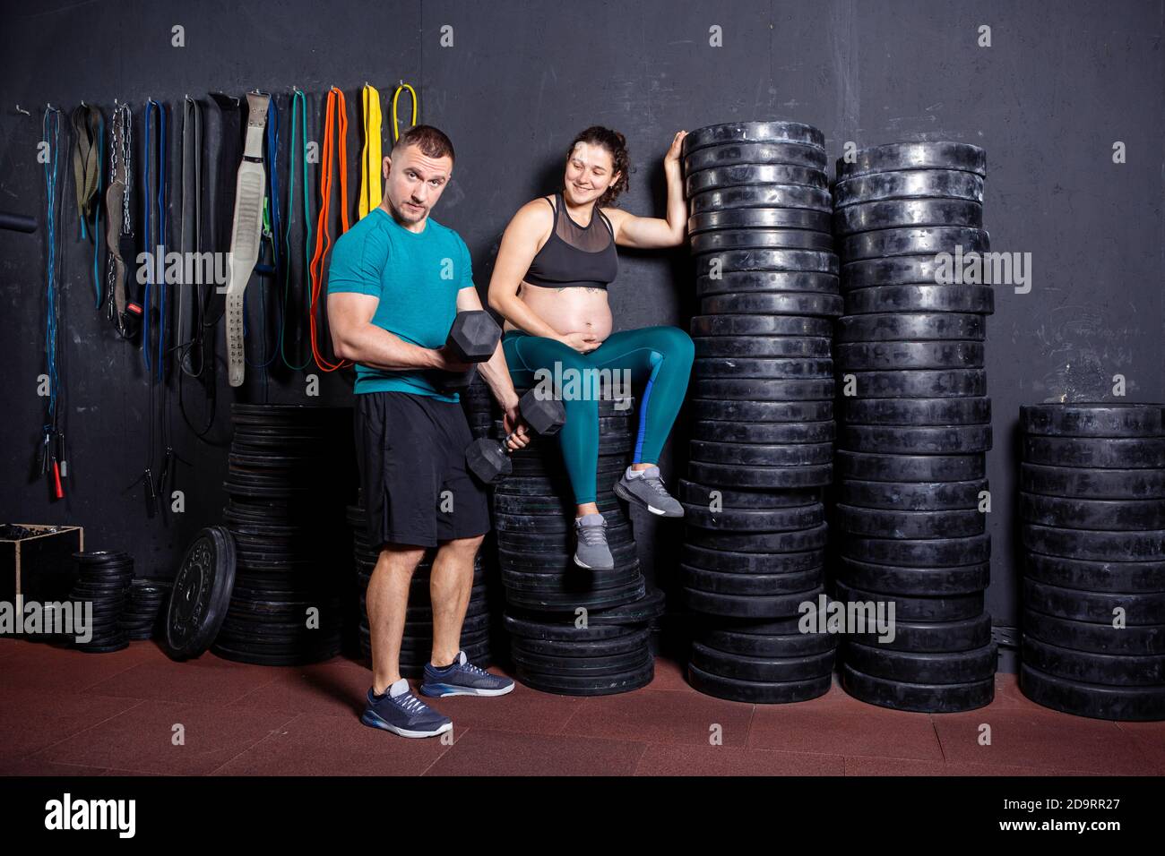 Periodo di gravidanza in donne forti muscolari atletiche. Allenamenti congiunti ed esercizi della coppia durante la gravidanza in palestra. Uomo e donna incinta Foto Stock