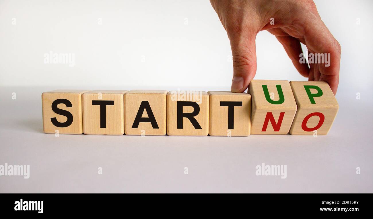 La mano maschile capovolge i cubetti di legno e cambia l'iscrizione 'start no' in 'start up'. Splendido sfondo bianco, spazio per la copia. Concetto aziendale. Foto Stock