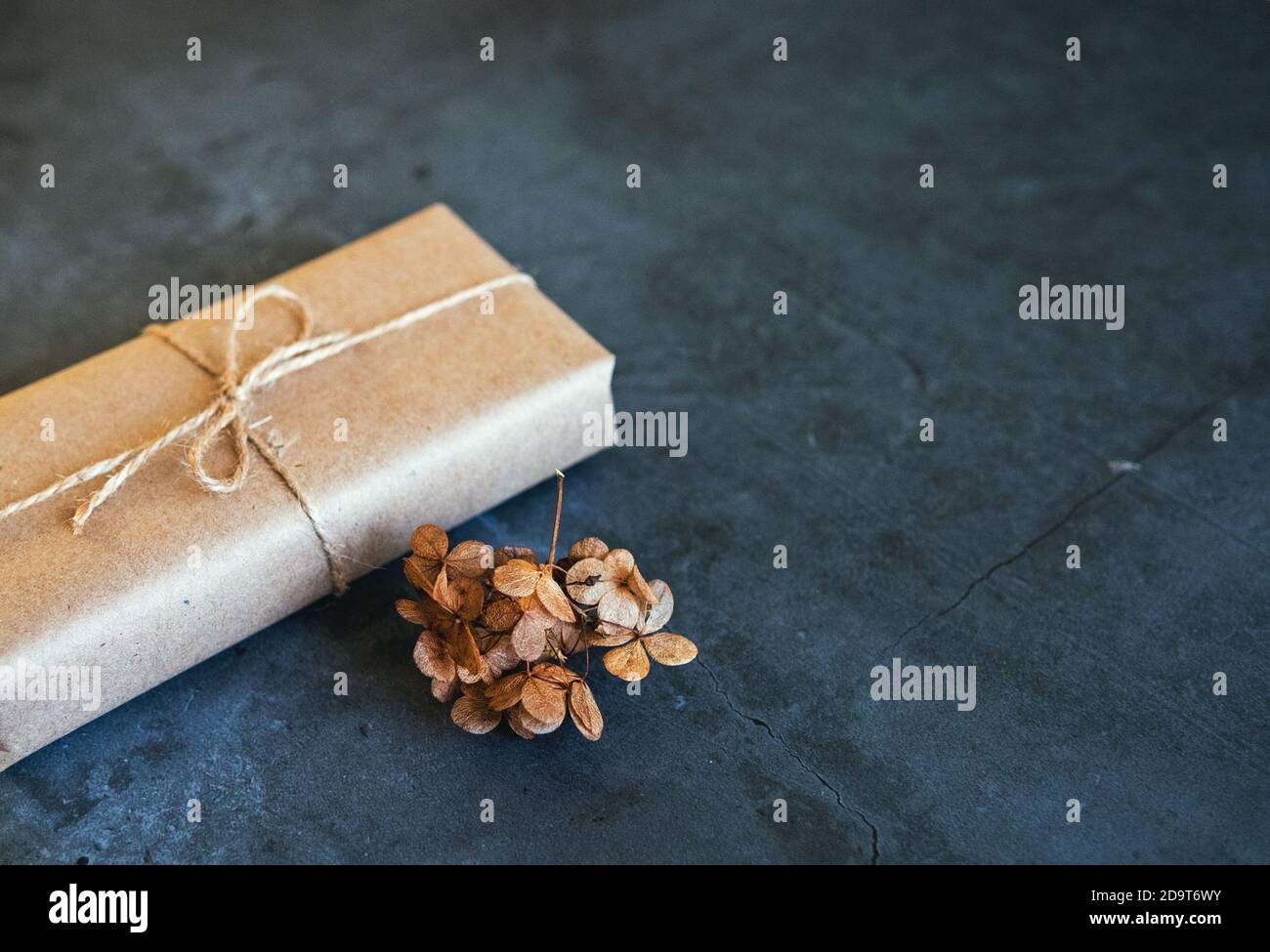 Confezione regalo avvolta in carta Kraft con fiori di idrangea essiccati, pampas essiccati su fondo scuro. Nuovo decor alla moda, spazio copia Foto Stock