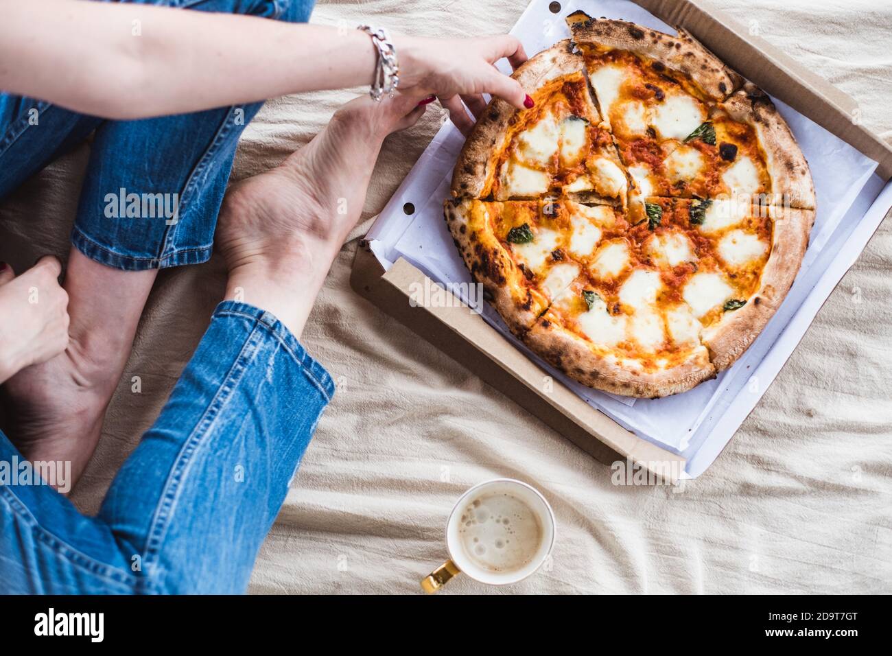 Ragazza seduta sul pavimento su una coperta con una tazza di caffè e una pizza, vista dall'alto Foto Stock