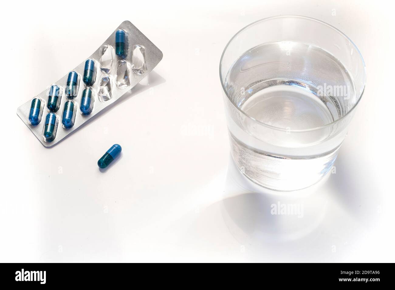 confezione blister di pillole blu e un bicchiere d'acqua su sfondo bianco Foto Stock