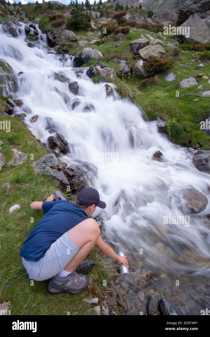 ragazzo che riempie una bottiglia d'acqua in un fiume di montagna In Pirenei verticali Foto Stock