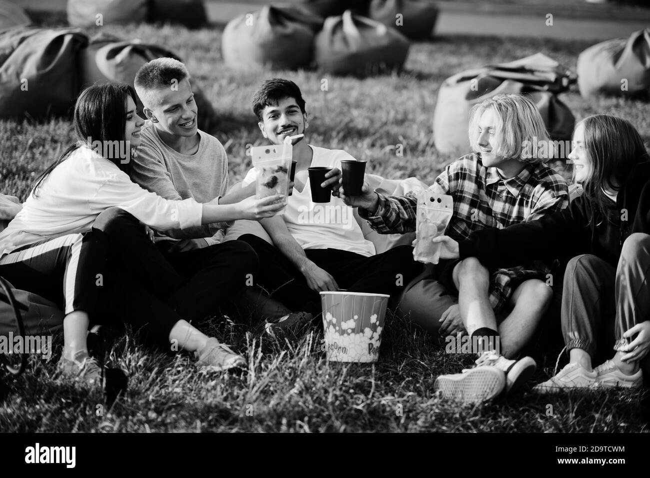 Giovane gruppo multietnico di persone che guardano film in poof al cinema all'aperto e bevono. Foto Stock