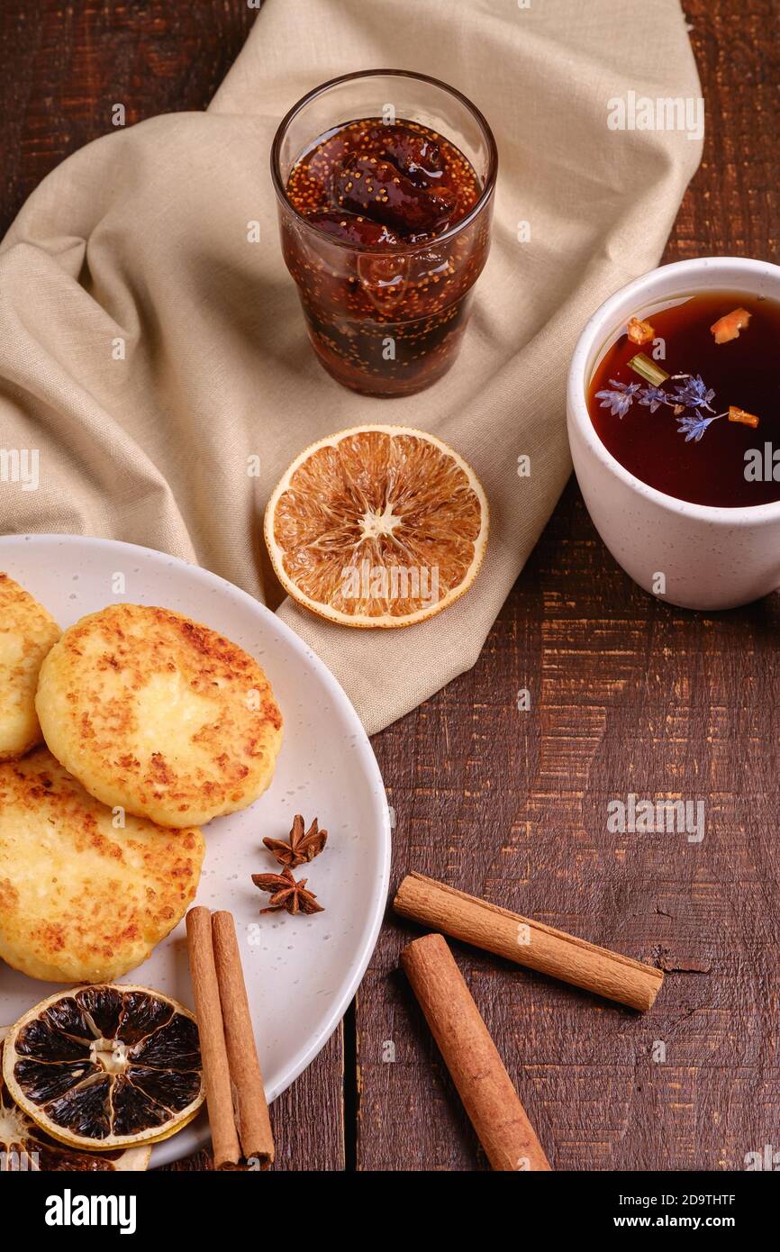 Frittelle di formaggio di cottage con tè nero aromatico caldo con confettura di fichi, umore della colazione di Natale con anice, cannella e agrumi secchi su sfondo di legno, Foto Stock