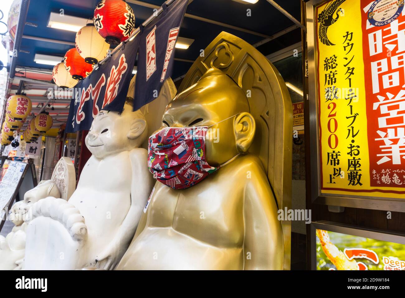 Statua del personaggio Billiken all'esterno di un ristorante nell'area di Shinsekai di Naniwa-ku, Osaka, Giappone che indossa una maschera durante la pandemia COVID-19 Foto Stock