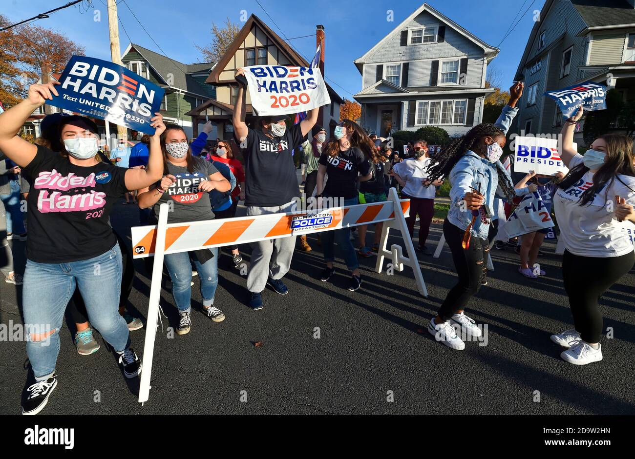 La gente che indossa la maschera mentre tiene i cartelli celebrano sulla via di North Washington in Scranton.Joe Biden è stato sopportato e cresciuto in Scranton, lui il lunedì ha visitato la sua casa d'infanzia e ha lasciato un messaggio sulla parete della stanza della famiglia. I sostenitori sono venuti a casa a North Washington Street a Scranton dopo che Biden ha vinto le elezioni, un flusso costante di automobili che si guidano piangendo, salutando e ballando fuori casa sua. Foto Stock