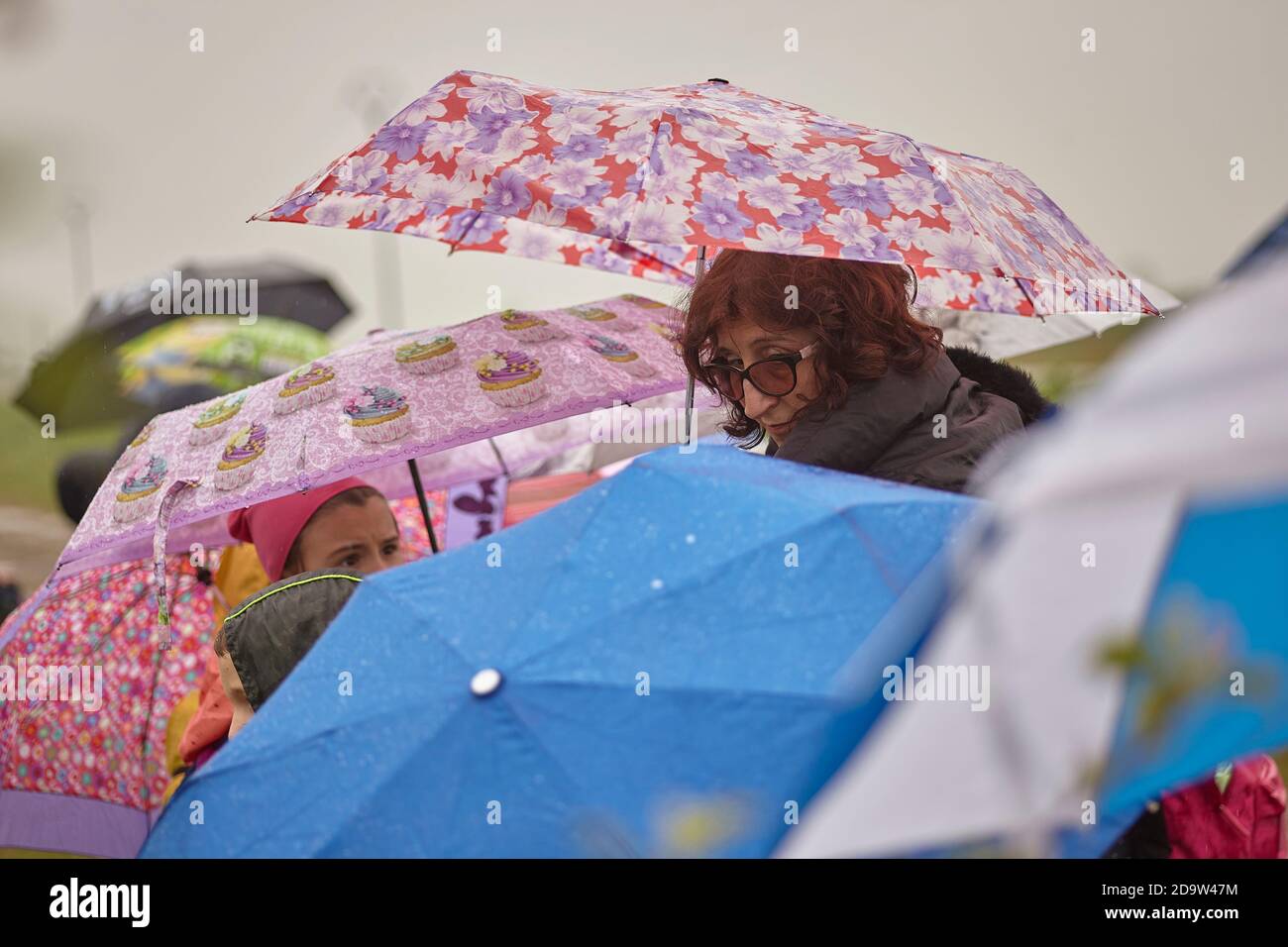 Folla di persone che camminano sotto la pioggia protetta da colori ombrelli e una donna si gira a guardare indietro Foto Stock