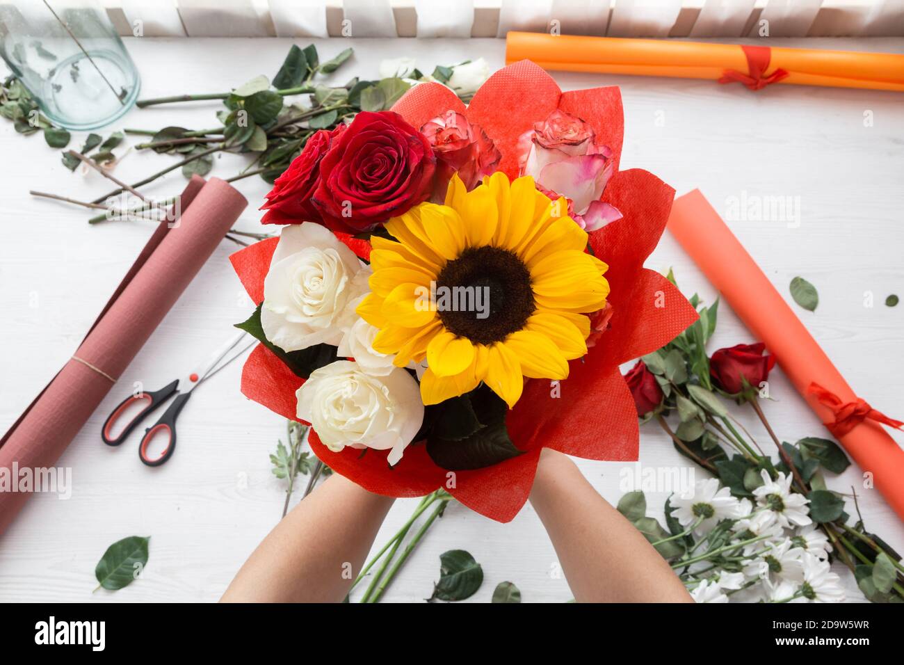 mani che tengono una disposizione bella del fiore fatta con le rose e girasole, nei cartoncini di sfondo e forbici Foto Stock