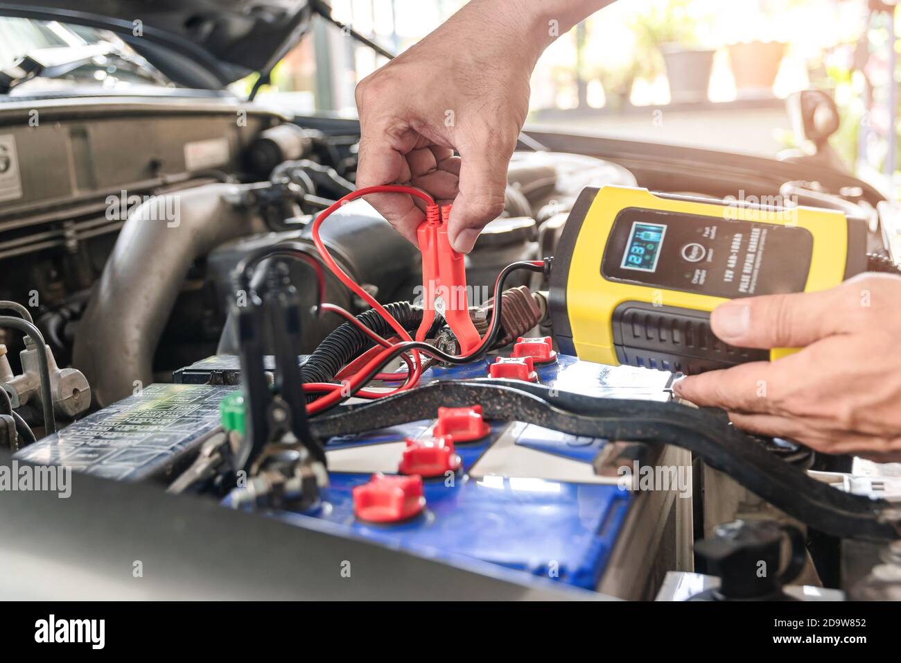 Il meccanico dell'auto sta utilizzando uno strumento di misurazione della tensione e sta caricando la batteria, l'alimentazione della batteria dell'auto. Foto Stock