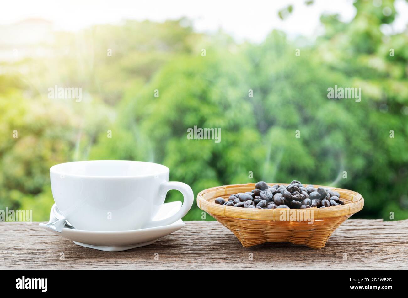 Tazza di caffè calda e chicchi di caffè nel piatto di bambù sul vecchio pavimento di legno con sfondo verde colorato della natura. Foto Stock