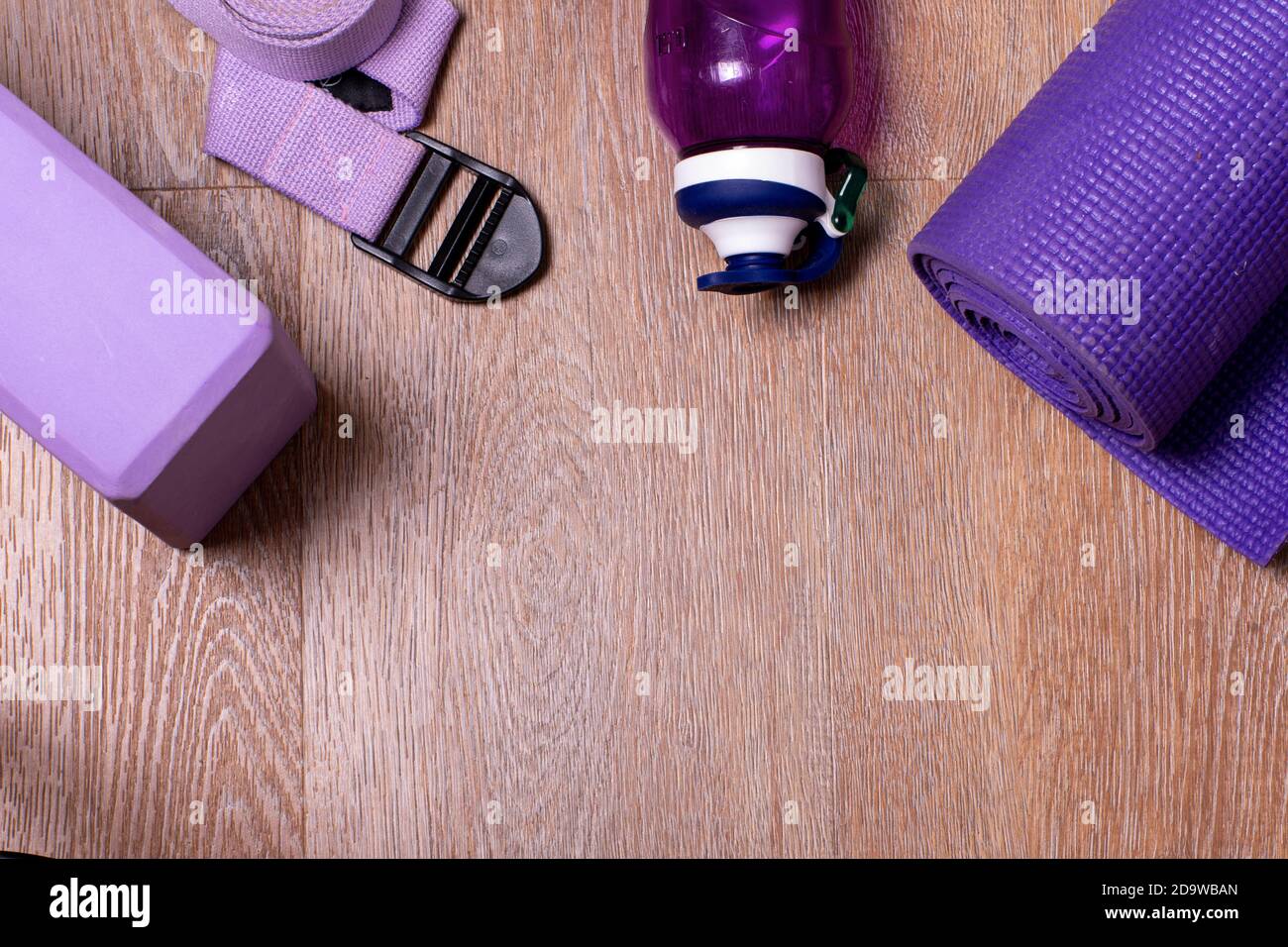 Bottiglia d'acqua piatta, tappetino, blocco, cinturino per yoga, fitness su sfondo di legno. Il concetto di uno stile di vita sano, sport e dieta. Messa a fuoco selettiva Foto Stock